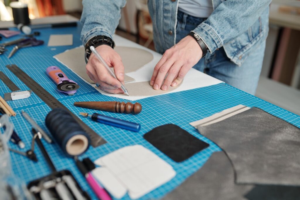 Young leatherworker in workwear outlining paper pattern over piece of suede